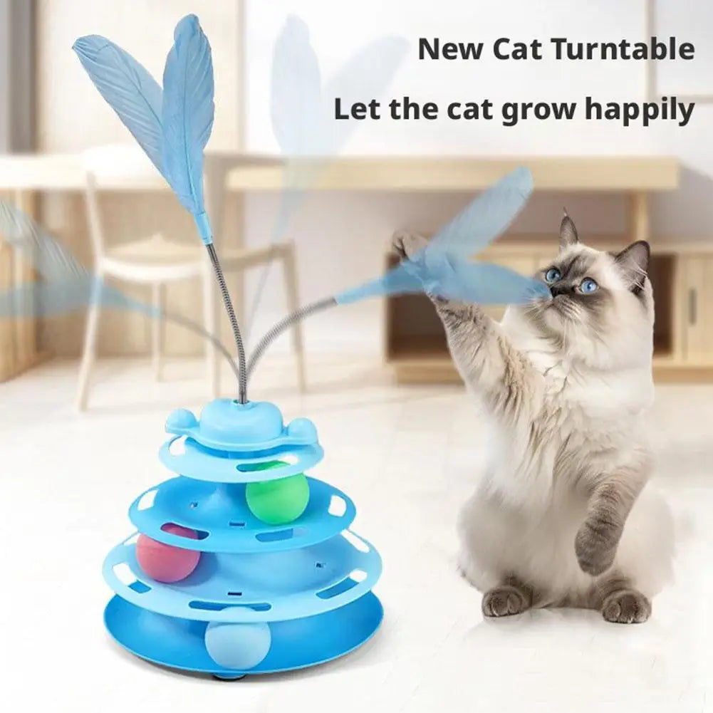 A fluffy gray cat plays with a blue interactive turntable toy tower featuring feather attachments.