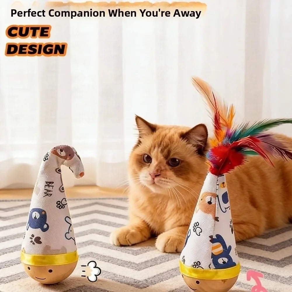 An orange cat sits next to a decorative toy featuring a bear design and colorful feathers.