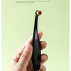 A hand holds a black pet tear stain remover brush with a soft, light brown tip.