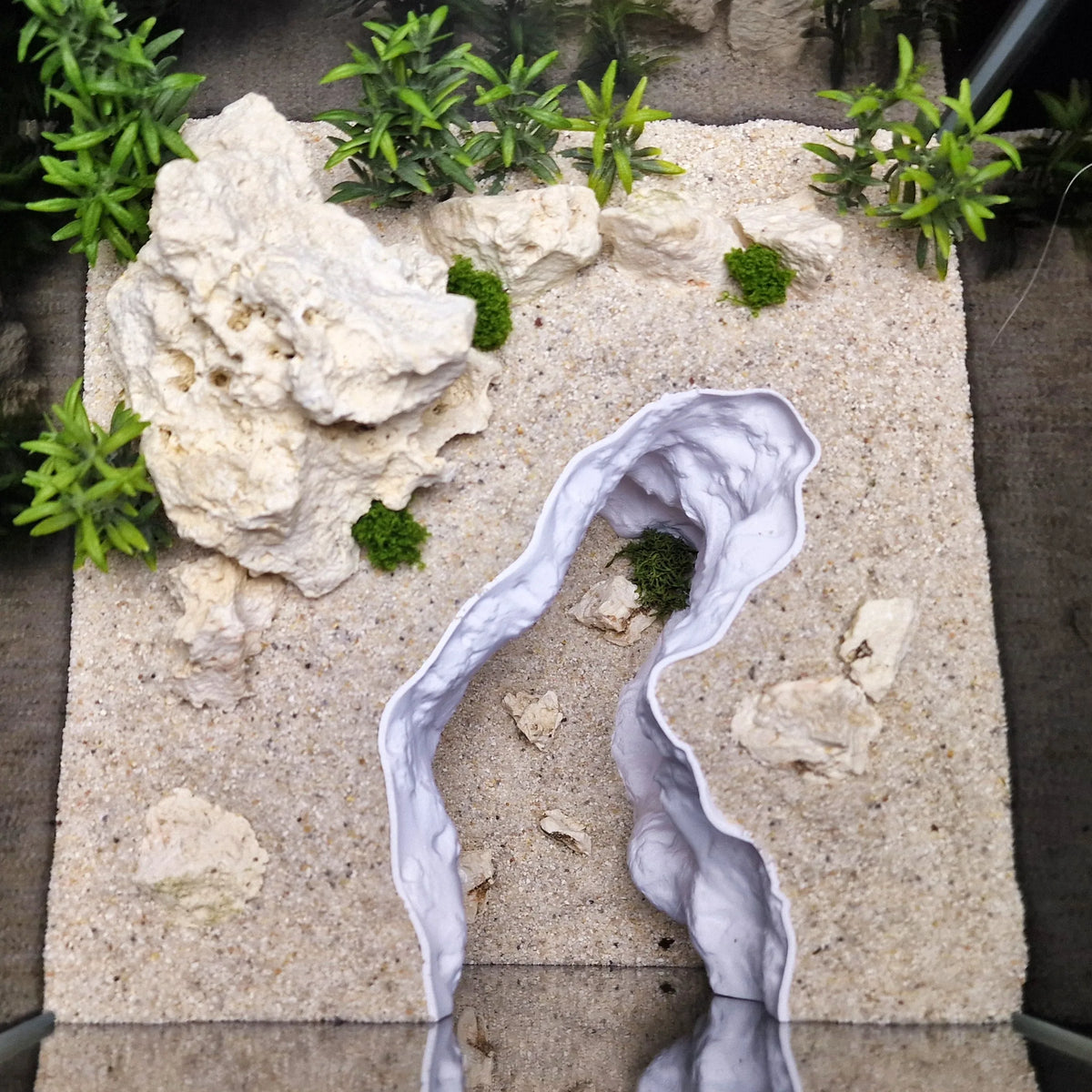 A 3D rock cave aquarium ornament featuring natural terrain design with white and green moss accents.