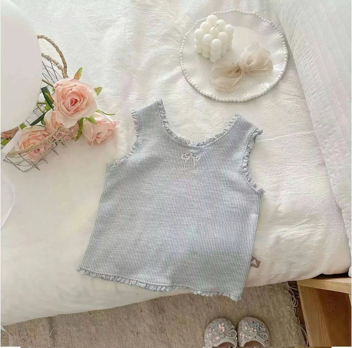 A light blue knitted mini vest with lace trim and a small embroidery detail displayed on a white surface.