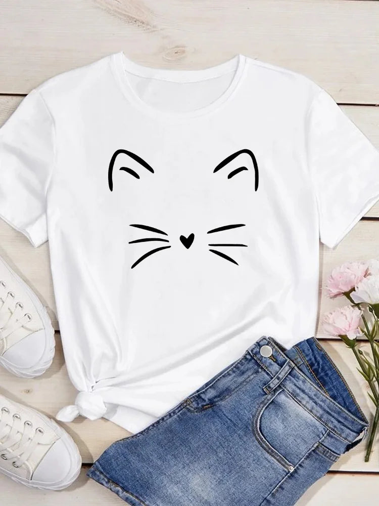 Camiseta blanca con un dibujo simple de la cara de un gato en línea negra sobre un fondo de madera clara.