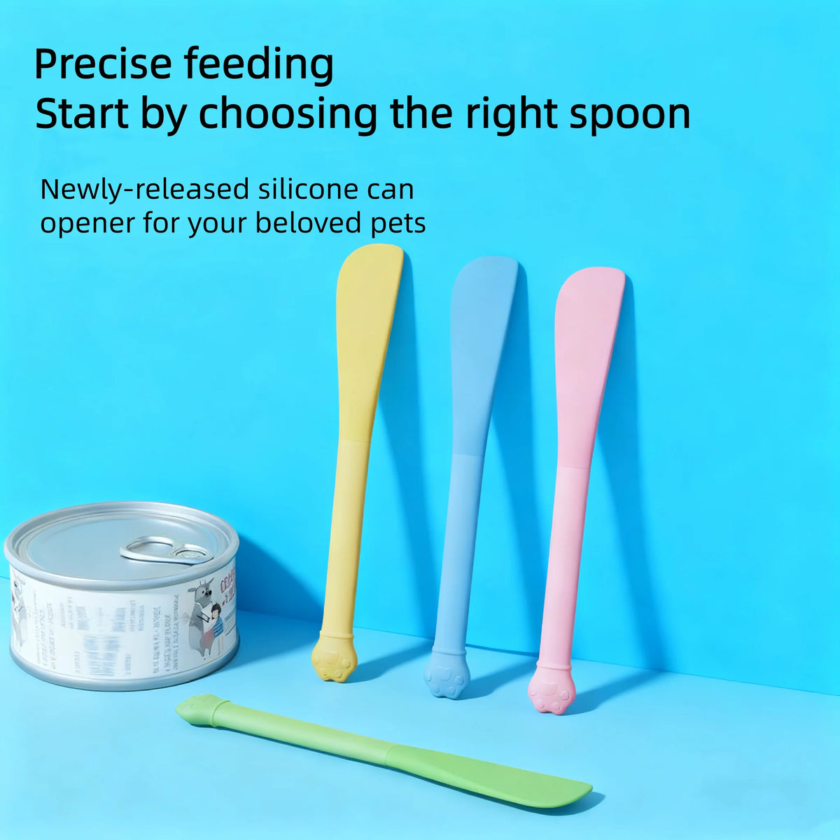 A set of colorful silicone pet feeding spoons, including a yellow, blue, and pink spoon, next to a metal can.