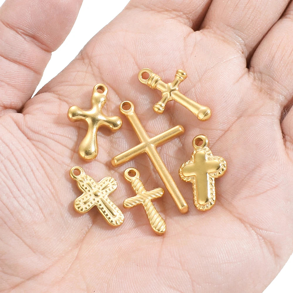 A set of vintage gold-toned cross charms for DIY jewelry making displayed in a person's hand.