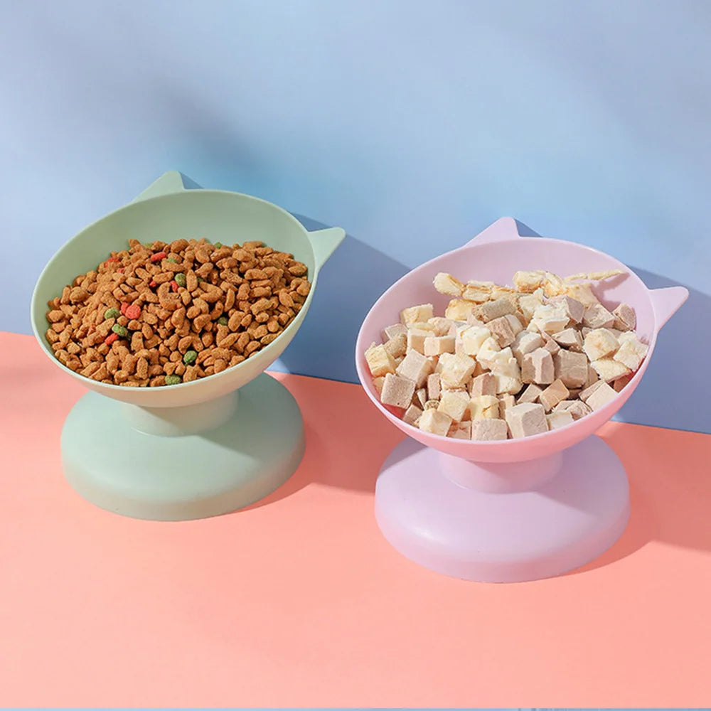 A pink pet food bowl with a non-slip base is filled with dry kibble, set against a light blue background.