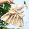 A yellow and white plaid reusable dog harness dress being held by a hand against a green outdoor background.