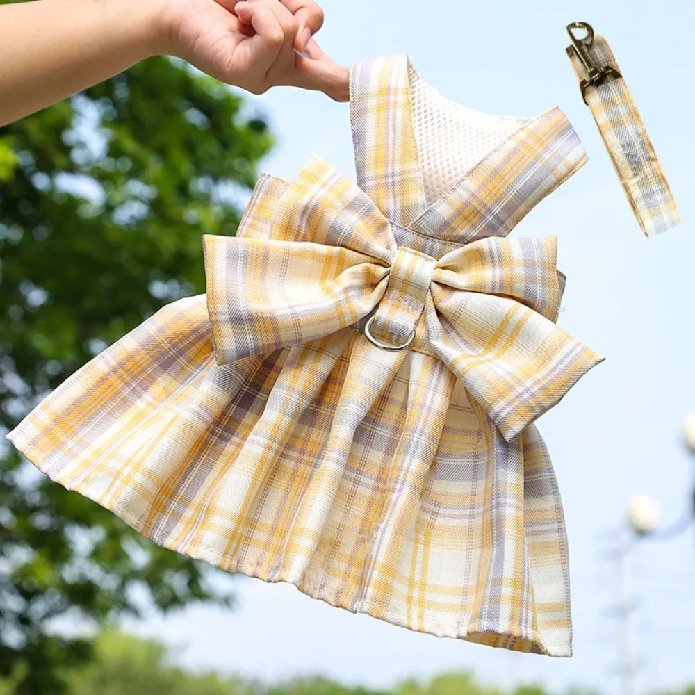 A yellow and white plaid reusable dog harness dress being held by a hand against a green outdoor background.