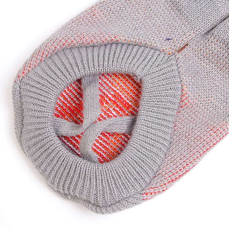 Primer plano de un acogedor suéter tejido para mascotas gris con detalles rojos, mostrando la textura de punto.