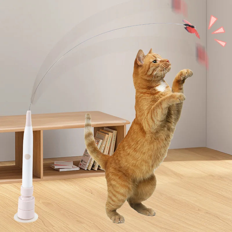 An orange cat is playing with an electric rotating butterfly toy that is being guided by a thin wire.