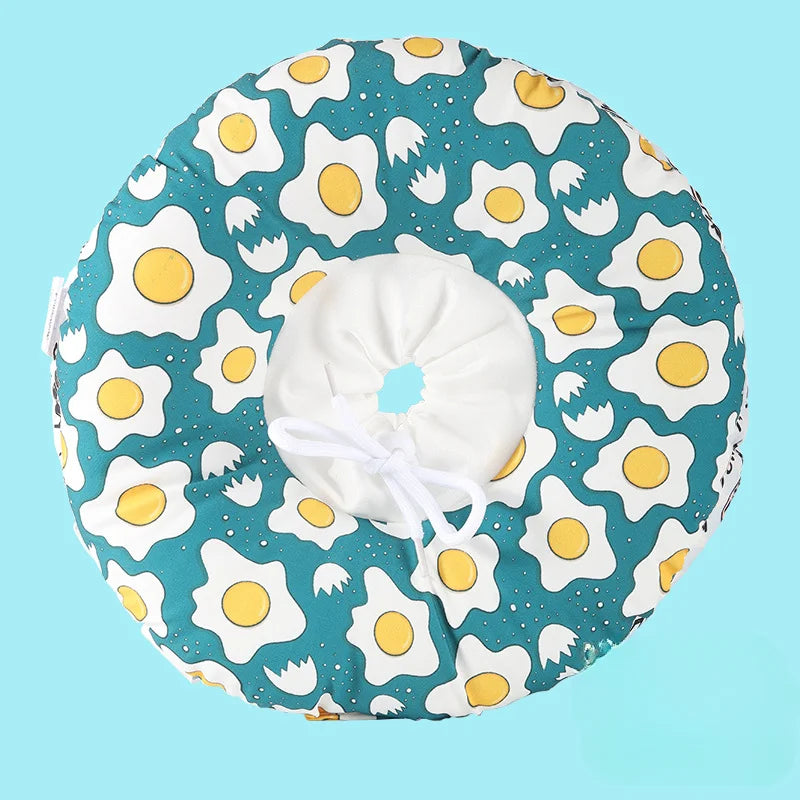 A round, blue fabric collar patterned with white and yellow stylized fried eggs for dogs or cats.