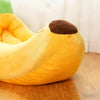 Un lit pour animal en forme de banane jaune avec une pointe marron, posé sur une surface en bois.