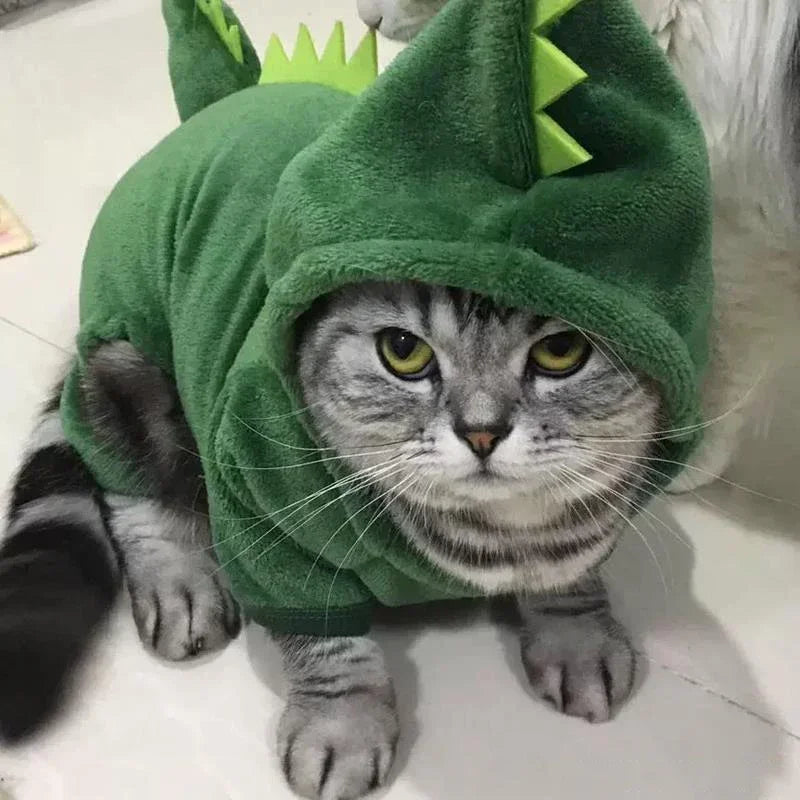 A tabby cat wearing a green cartoon animal costume jumpsuit with large eyes and pointed ears.