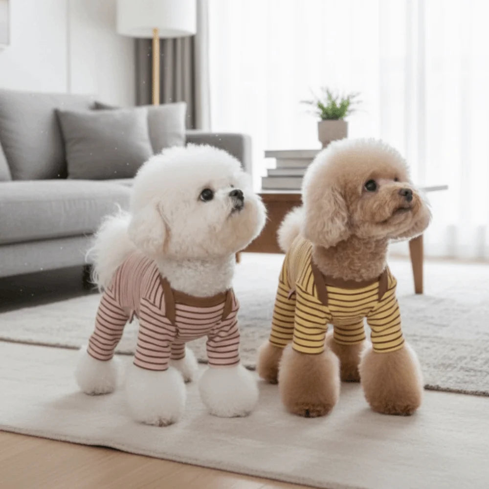 Two fluffy dog plush toys wearing cozy striped pajamas sitting on a light rug.