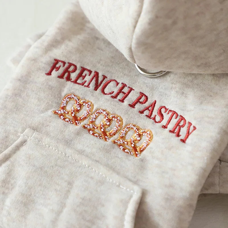 A light beige hoodie features red embroidery spelling out FRENCH PASTRY and a gold glitter design.