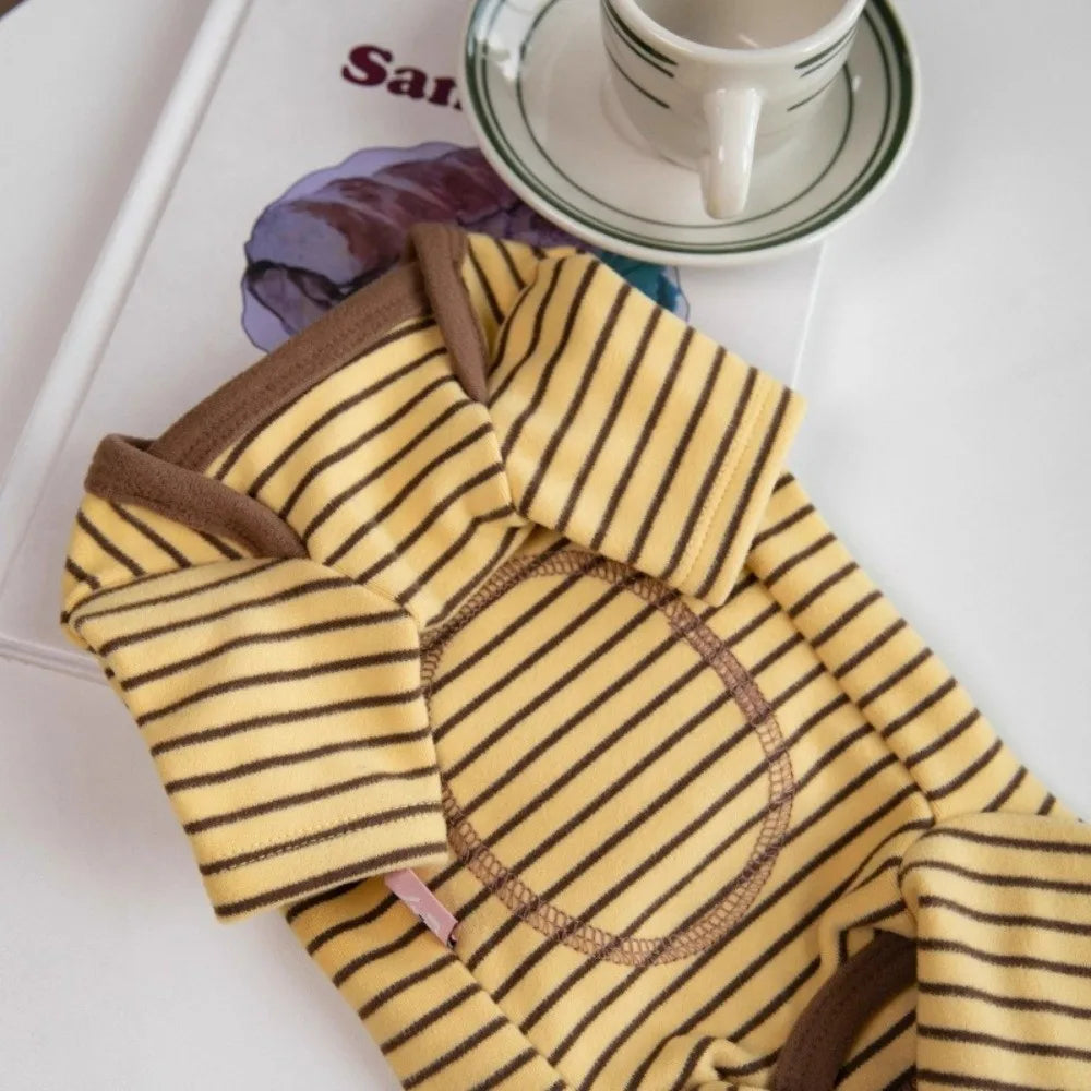 Yellow and brown striped dog pajamas laid out on a white surface next to a teacup.