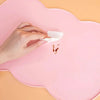 A hand is placing a piece of tissue onto a pink silicone pet feeding mat.