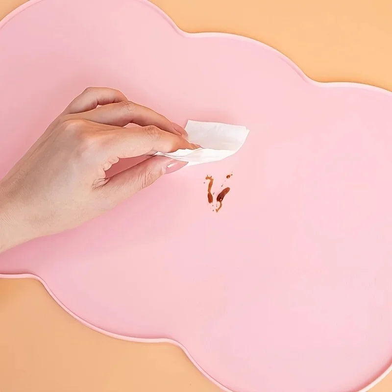 A hand is placing a piece of tissue onto a pink silicone pet feeding mat.