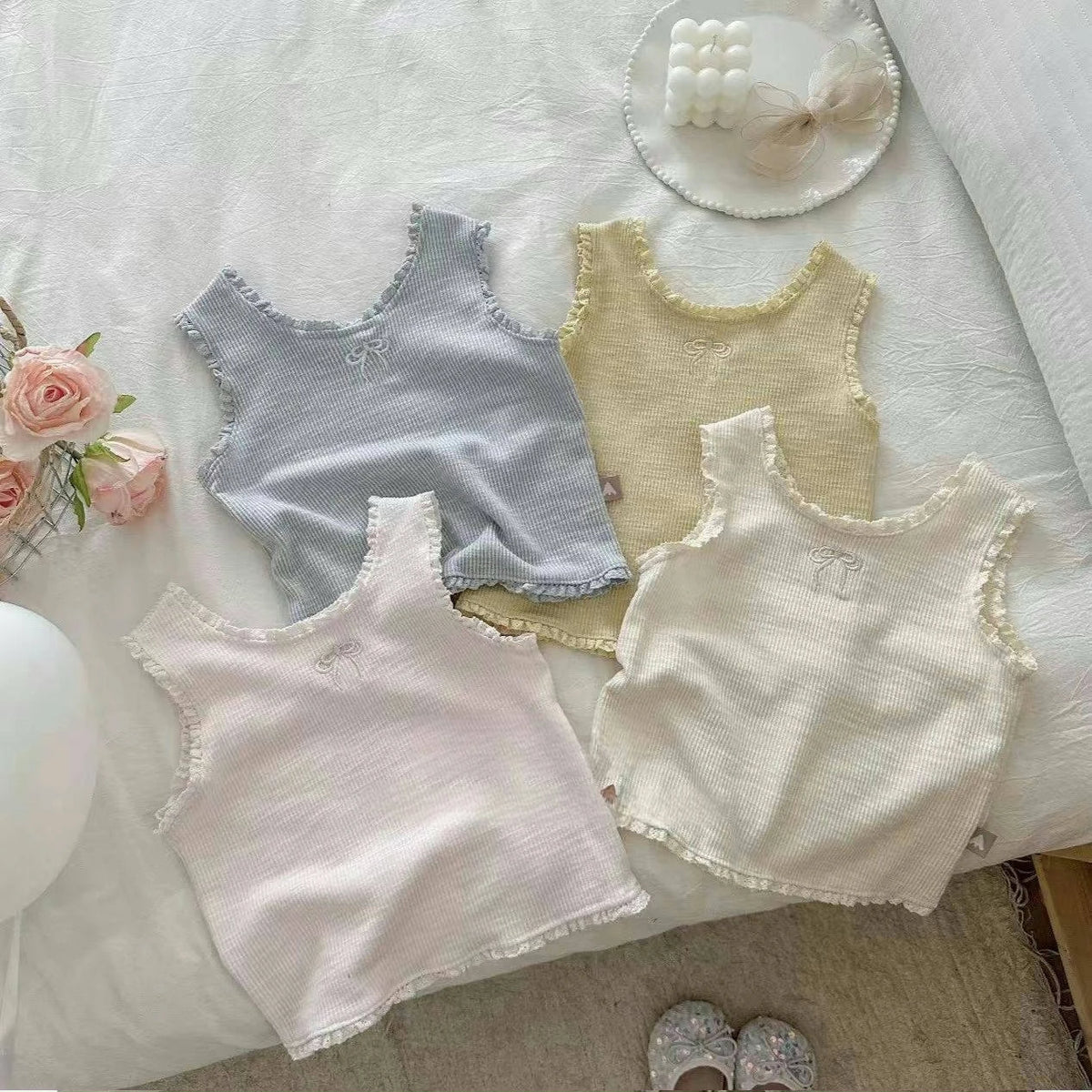 Three light colored mini vests with lace trim and embroidery displayed on a white surface.