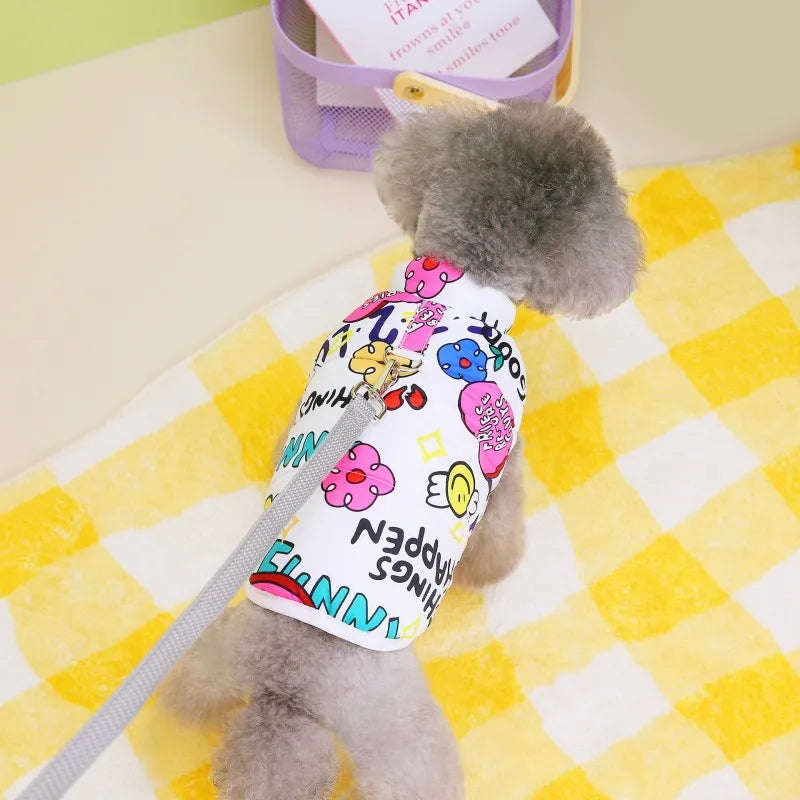 A gray dog wearing a white waterproof coat with pink and yellow patterns, lying on a yellow checkered blanket.