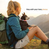 A person is holding a small dog with a silicone AirTag collar holder outdoors on a grassy hill.