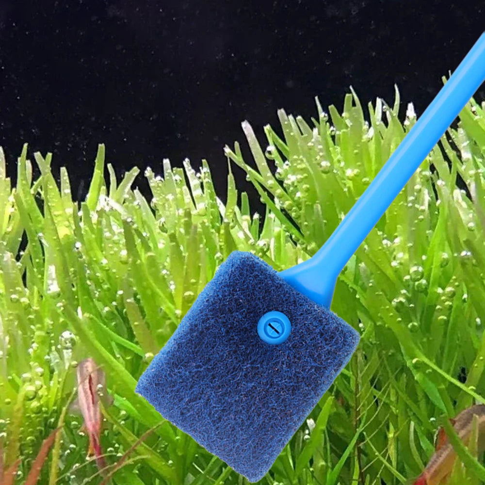 A blue dual-sided aquarium cleaning brush is shown resting on bright green aquatic plants.