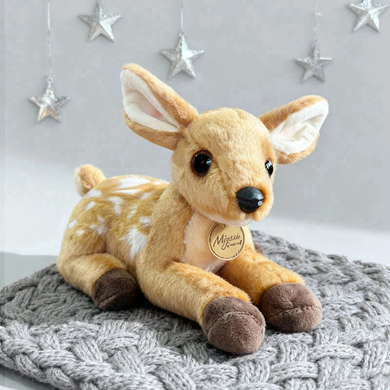 A soft plush giraffe stuffed animal toy with light brown fur and large ears sitting on a gray knitted surface.