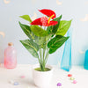 A vibrant red artificial anthurium plant in a white pot displayed on a white surface.