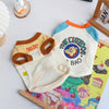 A white dog vest t-shirt with blue and orange trim, featuring a graphic of a dog's face.