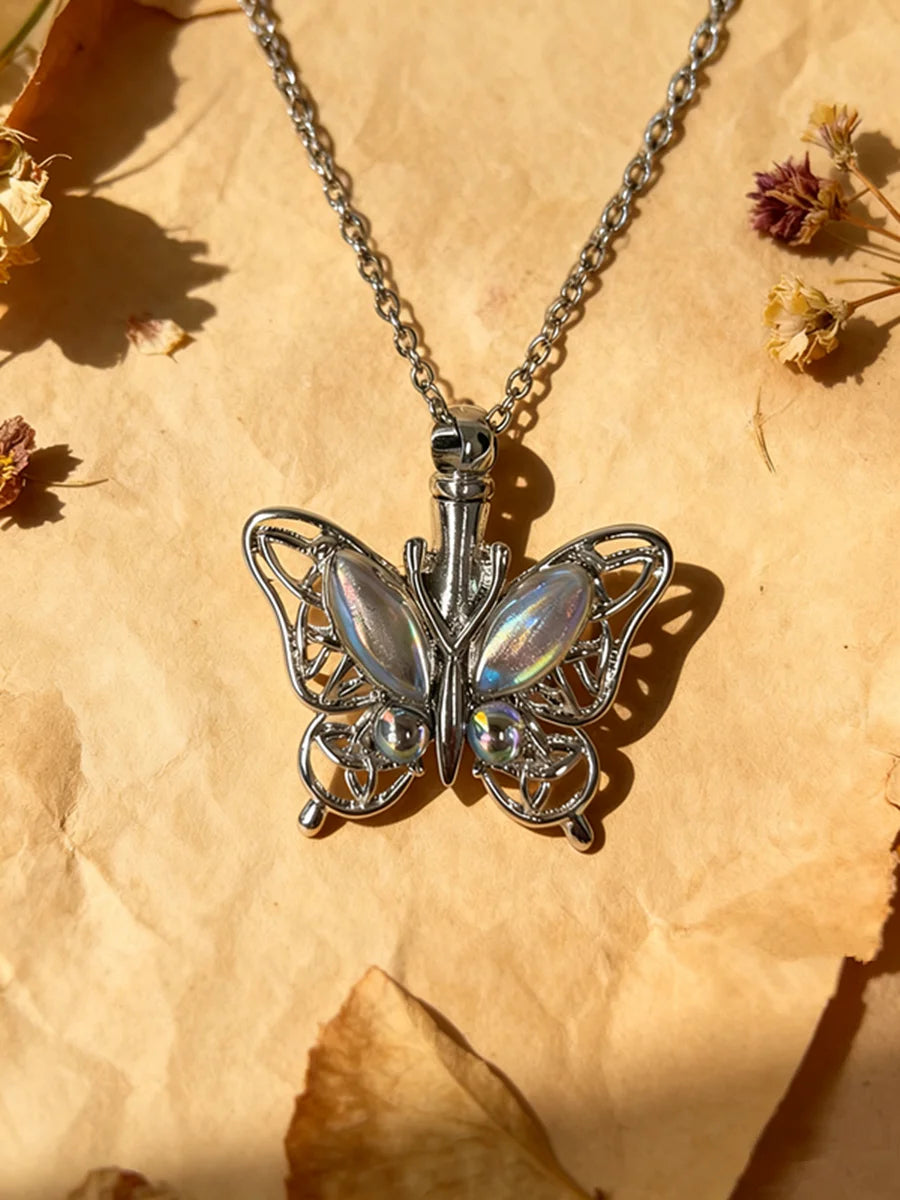 Silver butterfly ashes pendant necklace hanging from a chain on parchment paper