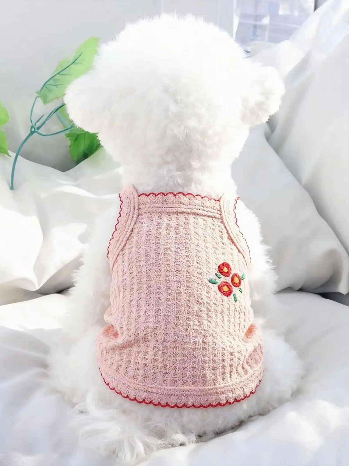 Collar de perro de peluche blanco y esponjoso con tela de punto rosa y ribete rojo, sobre una almohada blanca.