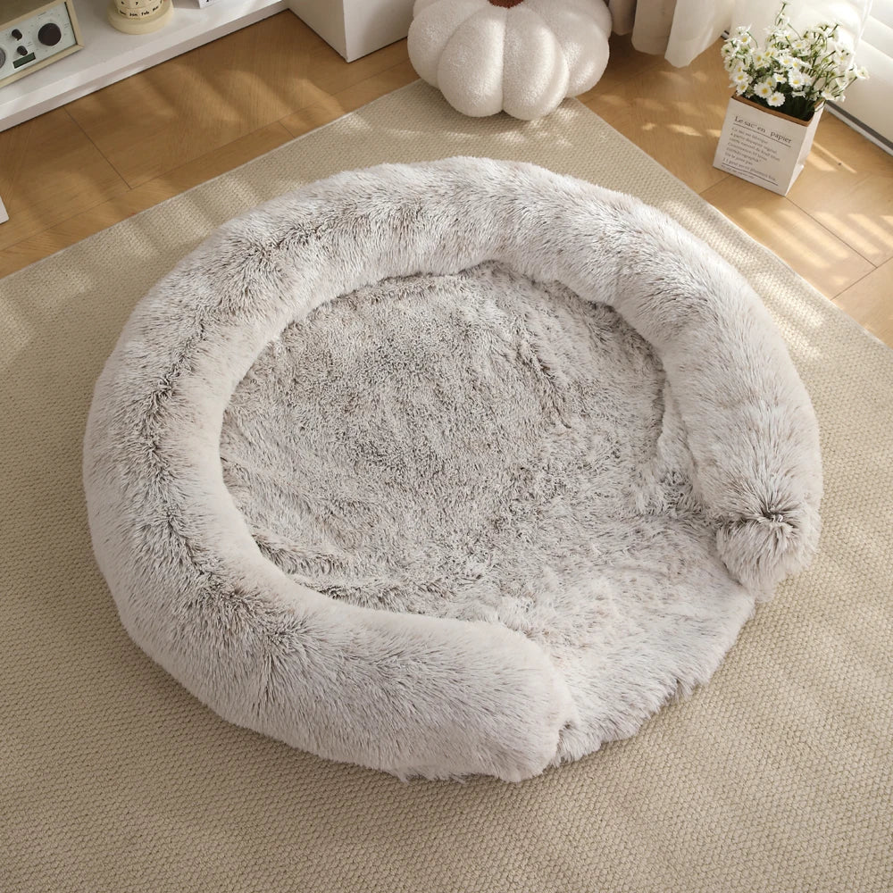 A round, ultra-soft, removable dog bed covered in fluffy gray faux fur resting on a light beige rug.
