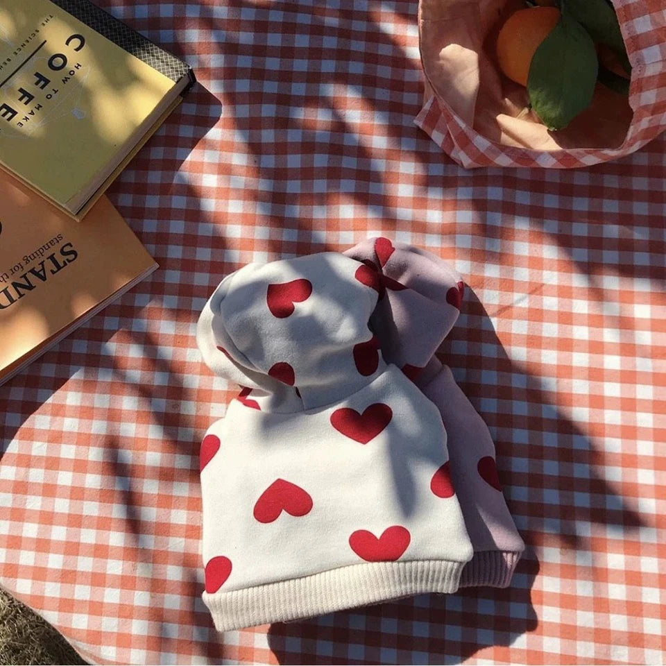 Weißes und pinkes Herzmuster-Teddy-Hoodie auf einem karierten Tisch mit Schatten.