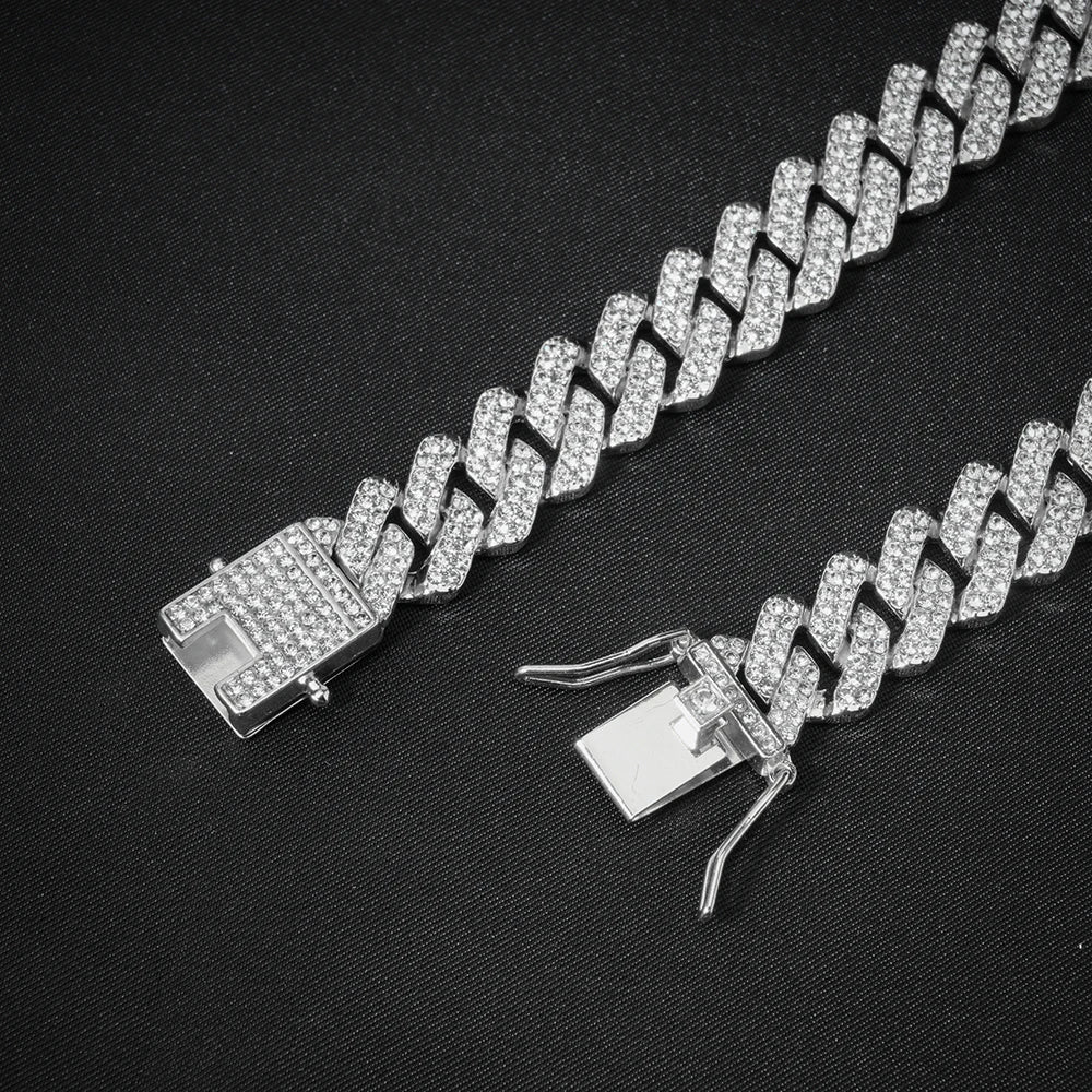 Rapproché d'un collier Cuban link argenté avec diamants pavés sur fond noir.