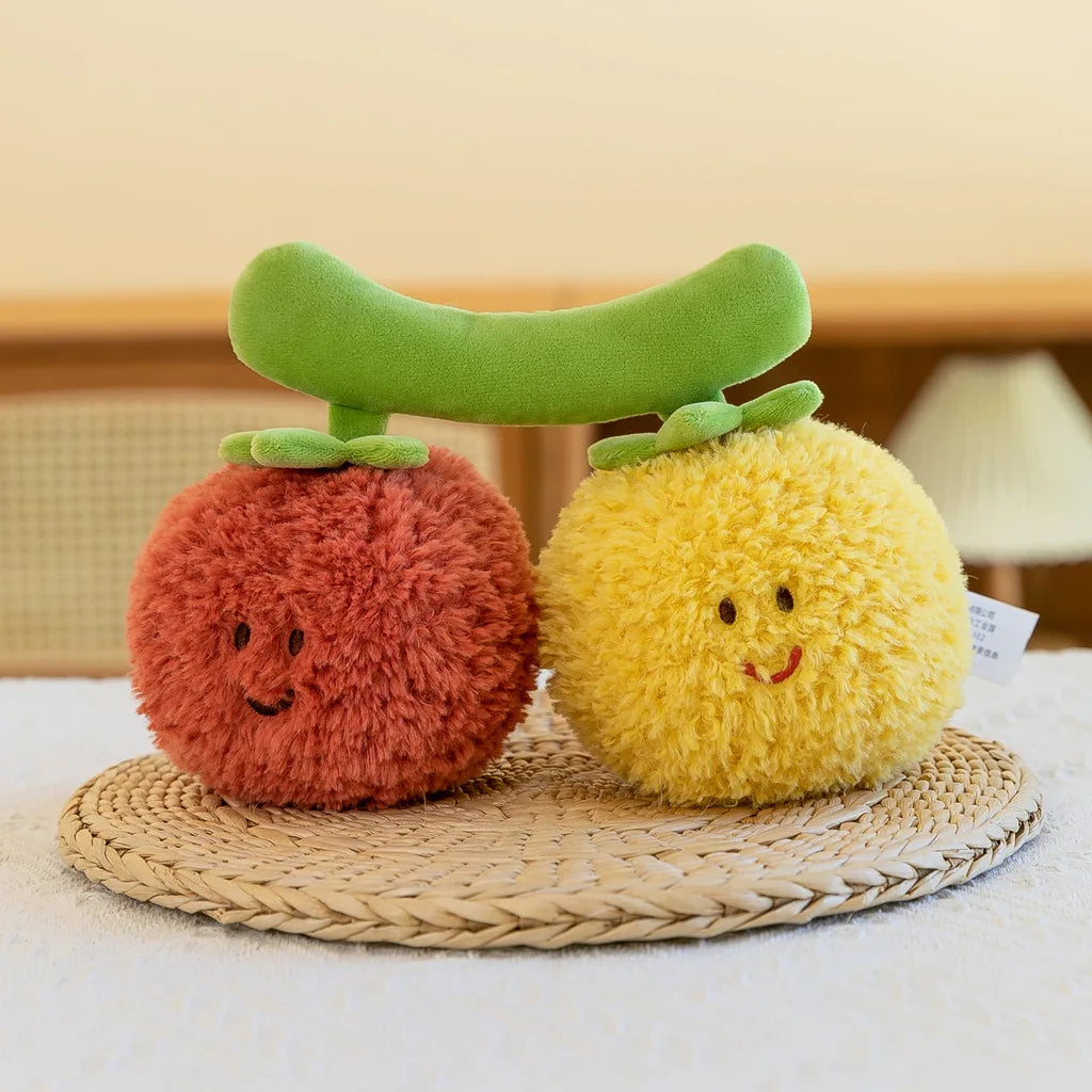 A set of soft plush vegetable dolls including a green broccoli, a red peanut, and a yellow mushroom resting on a woven mat.