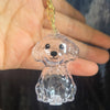 A clear glass dog pendant with floppy ears is held in a person's hand, attached to a gold-colored chain.