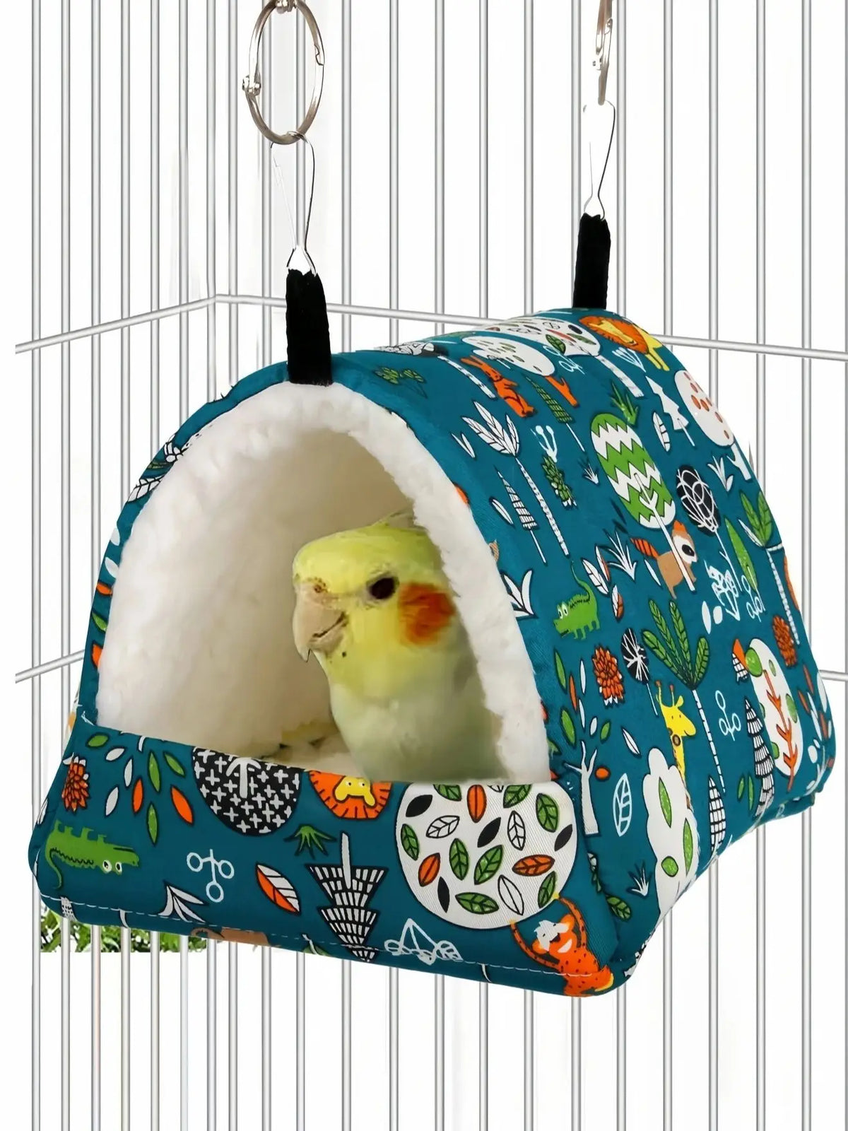 A colorful, fabric bird nest hammock with a rounded entrance hangs from a wire, featuring various natural and animal patterns
