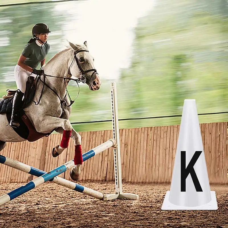 Un cheval et un cavalier effectuant des exercices de dressage avec des cônes blancs marqués de la lettre K.