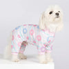 A white dog wearing a pink and blue animal print jumpsuit onesie.