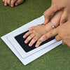 Kit d'empreinte de main montrant l'empreinte d'un bébé sur du papier blanc, avec une main humaine qui guide l'empreinte.