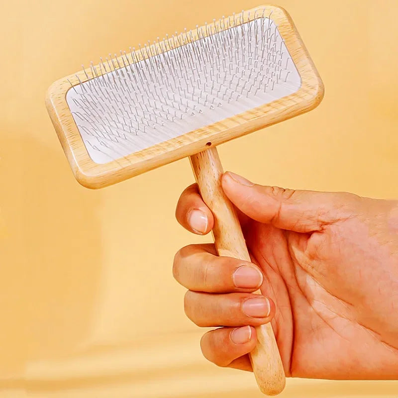 A hand holds a wooden pet grooming brush with massage bristles against a light yellow background.