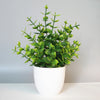 A potted artificial bonsai plant with bright green leaves sits on a white surface.