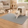 A white cat is standing on a gray honeycomb litter mat indoors.