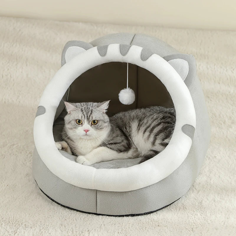 A gray cat cave bed with an arched entrance and a white fluffy pom-pom inside for a pet.