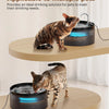 A tabby cat is drinking water from an automatic pet water fountain on a wooden surface.