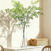 A tall glass vase filled with artificial bamboo stems, set against a light background.