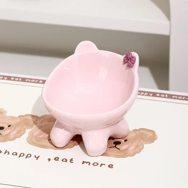 A pink ceramic cat food bowl with a raised, tilted design sits on a white surface.