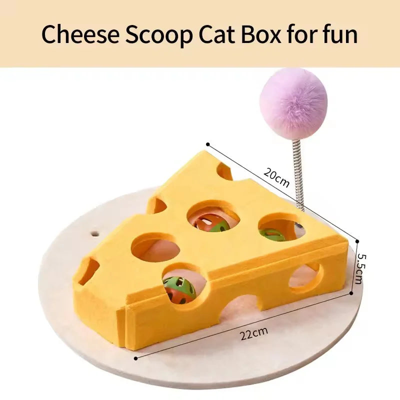 A yellow cheese scoop cat box for fun with holes and a pink felt ball on a white surface.