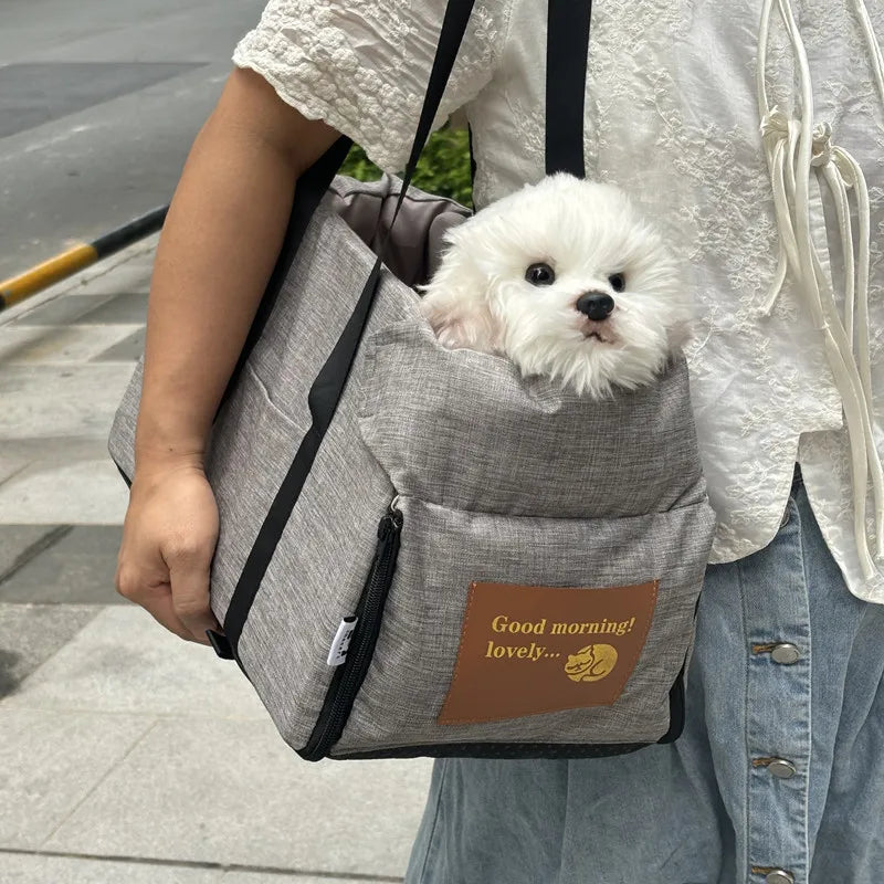 Eine Person trägt ein graues, tragbares Hundebett und -sitz mit einem flauschigen weißen Hund im Freien.
