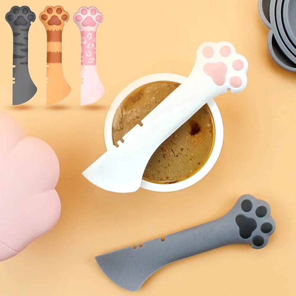 A collection of silicone cat paw shaped tools including a can opener and food scoop, shown next to a pink finger.