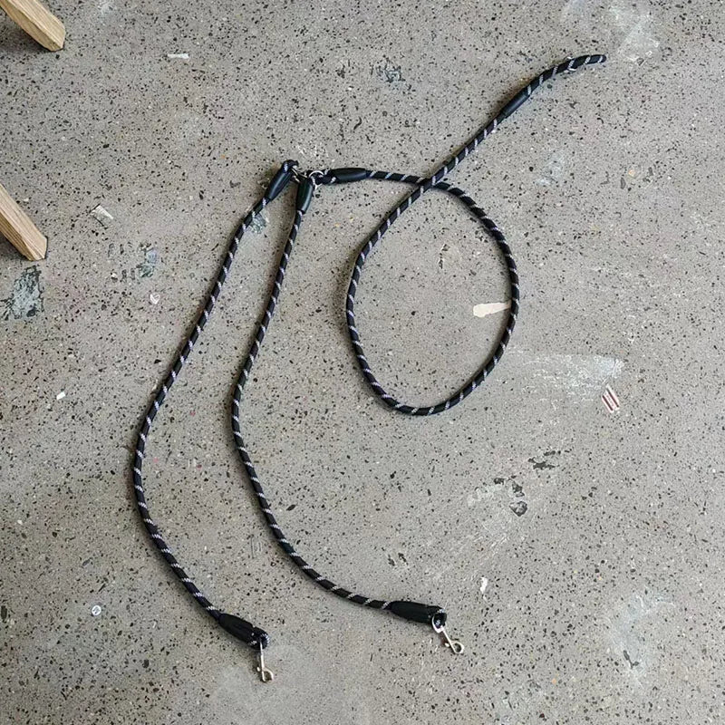 A black hands-free dog leash with a reflective stripe is laid out on a gray concrete surface.